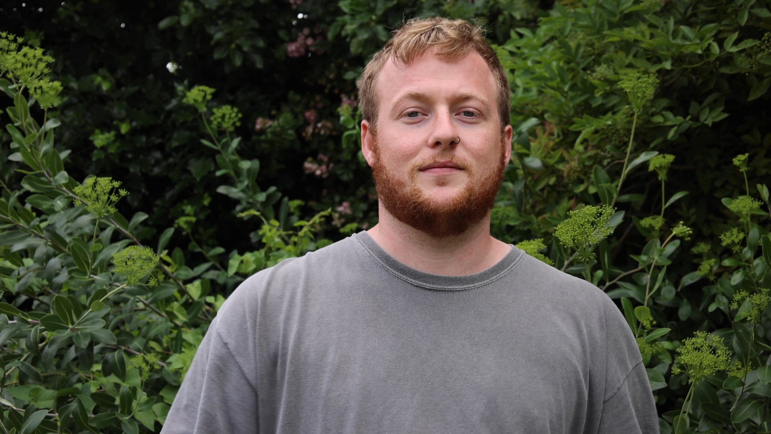 3/4 portrait of Dan Thatcher in a grey t-shirt with a green background
